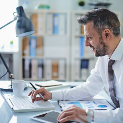 Man working simultaneously on a laptop, tablet, and clipboard